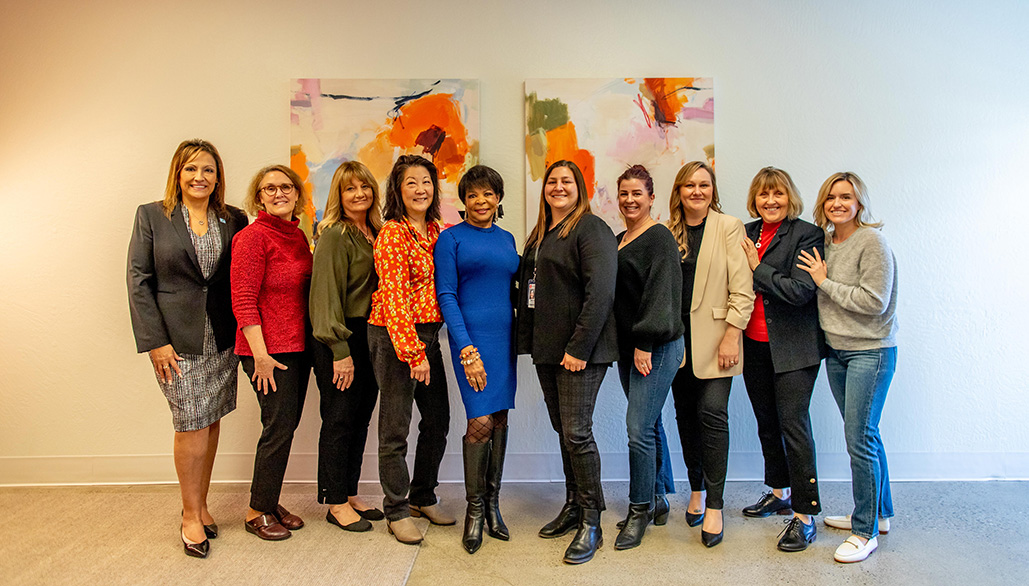 women standing in front of white wall with colorful paintings. Women are smiling and posing for photo.